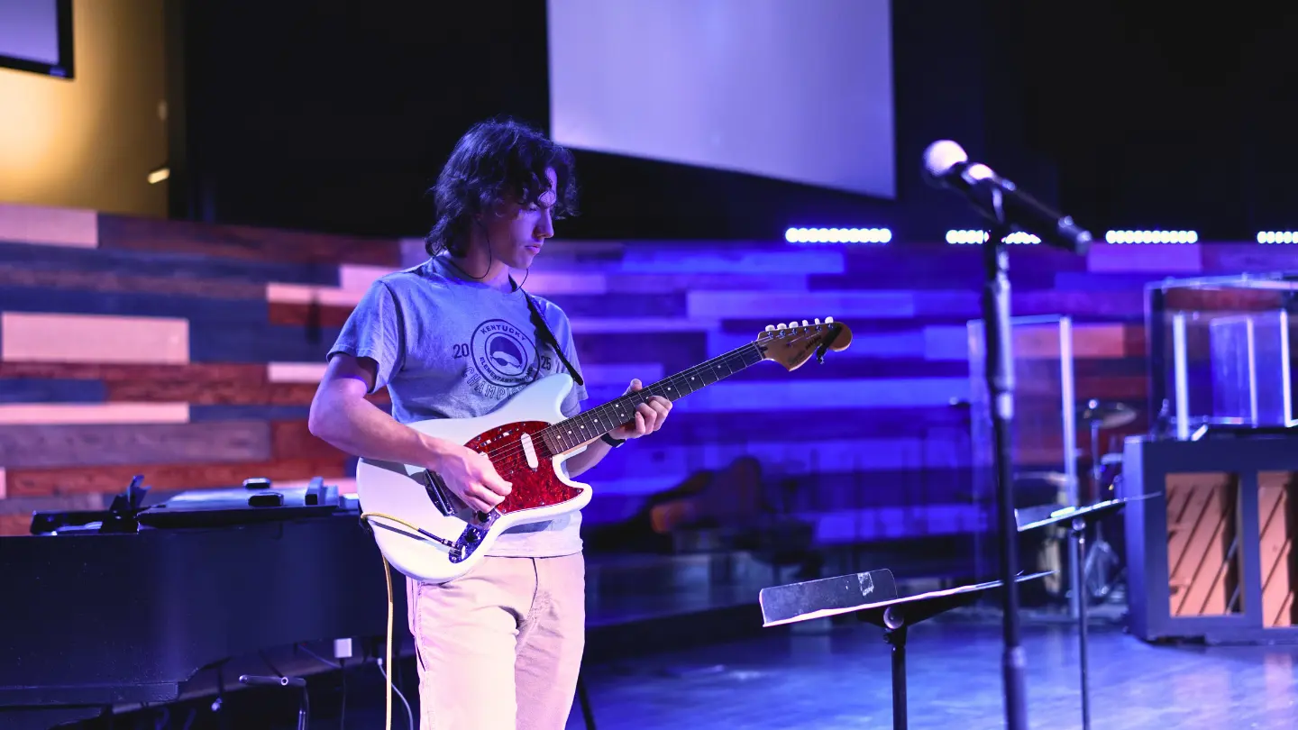 Jonah playing guitar on the stage in the auditorium at Immanuel Baptist Church Corbin Campus