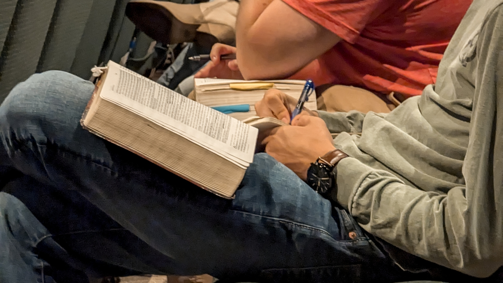 A close up of a young man's hands ands, Bible, and notebooks taking notes during church