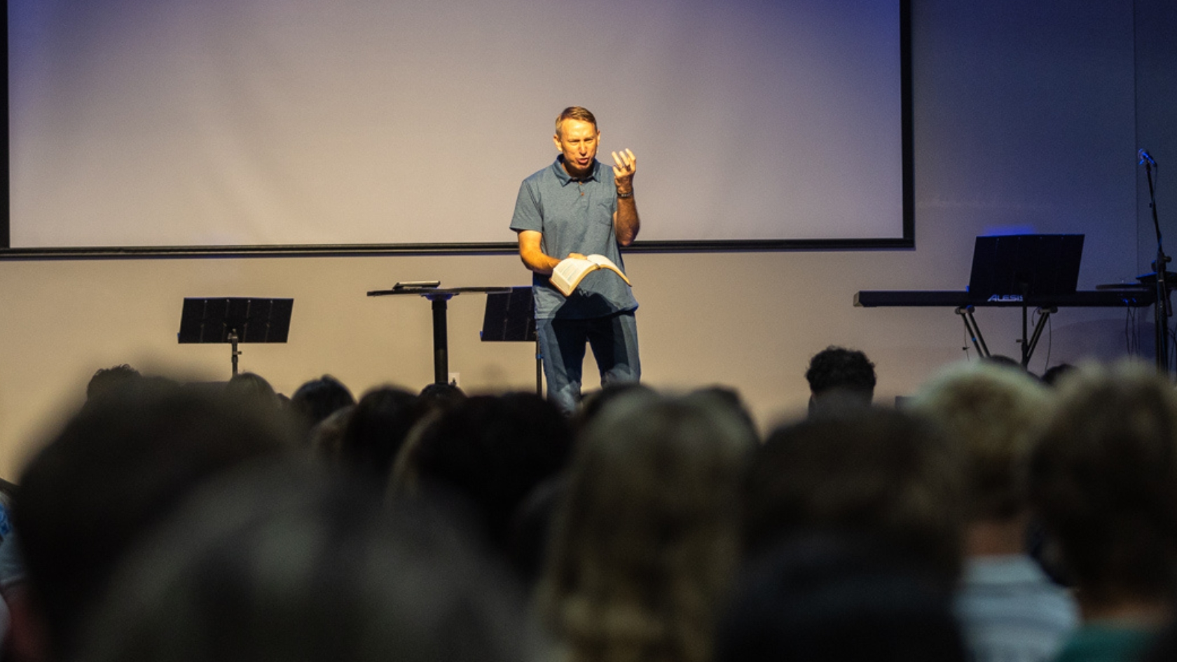 Pastor Allen Bonnell preaching to a congregation while holding an open Bible